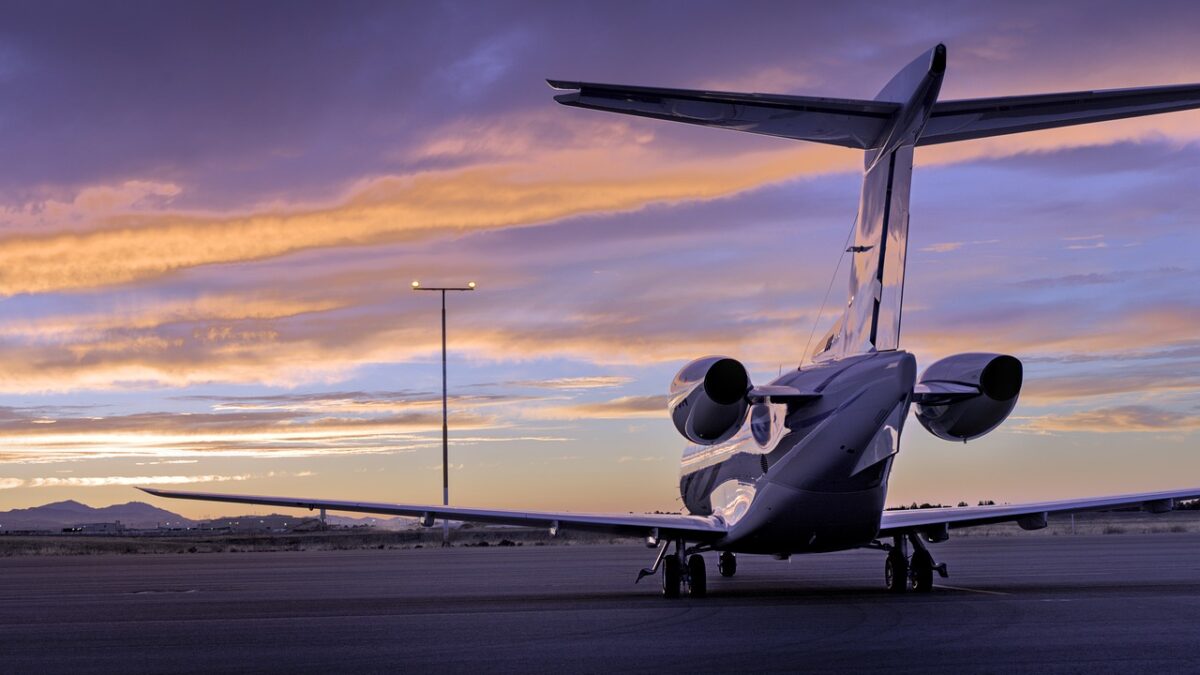 Jet d'affaires garé sur un tarmac au coucher du soleil, vu de l'arrière, avec empennage en T et deux réacteurs à l'arrière du fuselage. Ciel violet et orangé, lampadaire et collines à l'horizon.