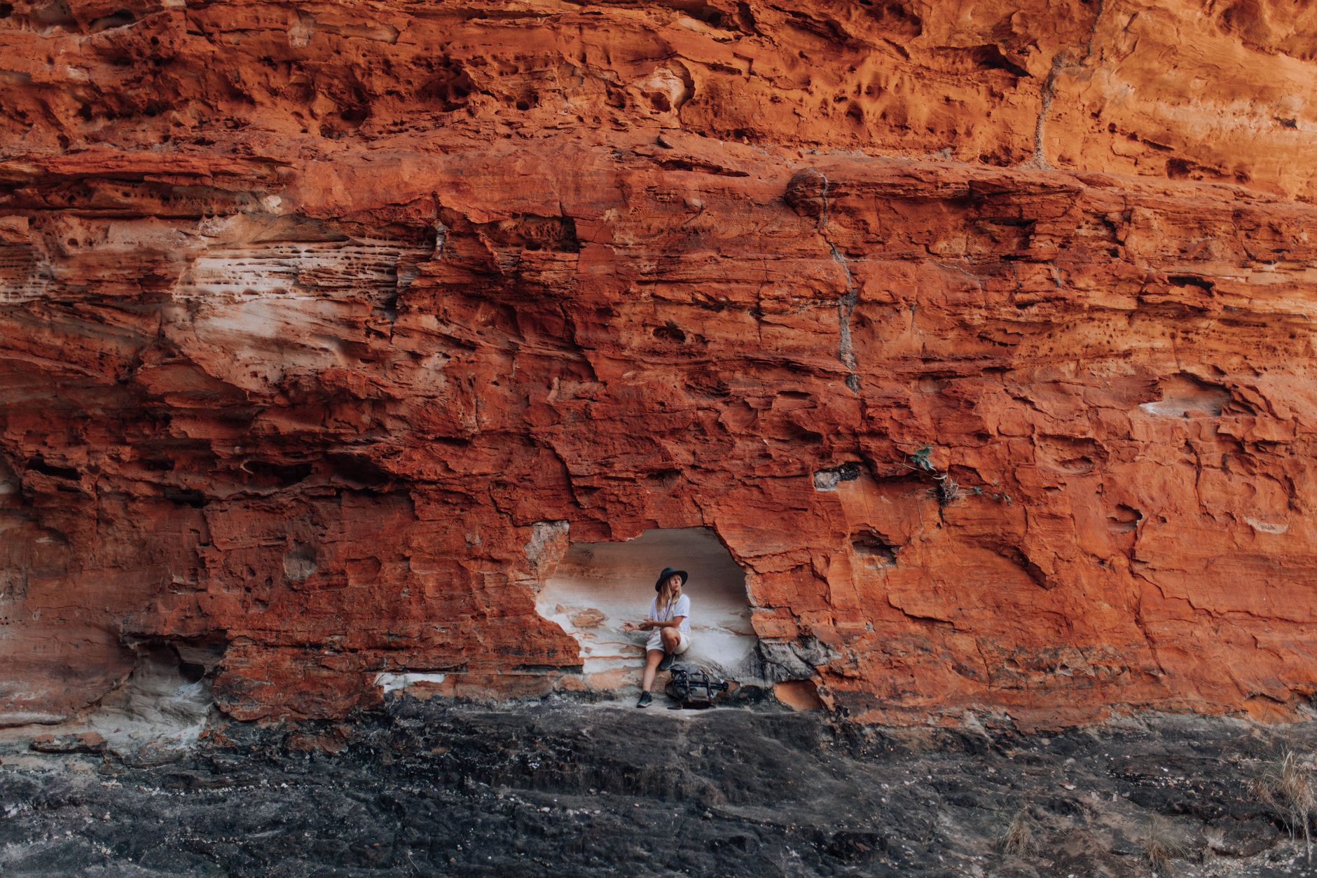 A traveler rests inside an opening in a massive red rock cliff face.